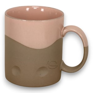 May include: A two-tone ceramic mug with a pink upper half and a brown lower half. The mug has a curved handle and a small embossed design on the side. The mug is designed for hot beverages.