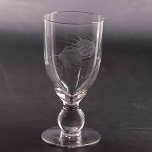 May include: A clear glass goblet featuring a delicate etched design of two clusters of grapes with thin, sweeping lines. The stem includes a prominent spherical ball detail above a circular base, providing a balanced and structured appearance.