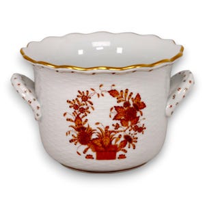 May include: A white porcelain bowl with a scalloped rim, two side handles, and a textured basket-weave surface. The exterior features a central orange floral motif, while the rim and handle edges are accented with a thin gold painted trim.