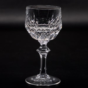 Könnte beinhalten: Ein klares Kristall-Weinglas mit facettierter Schale und Stiel. Das Glas hat einen runden Fuß und ein rautenförmiges Muster auf der Schale. Der Stiel hat ein geometrisches Design. Das Glas ist zum Servieren von Wein bestimmt.