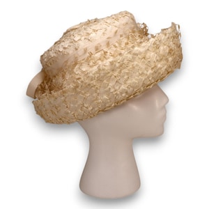 May include: A vintage cream-colored hat with a woven texture and a wide brim. The hat is displayed on a white mannequin head. The hat has a ribbon detail on the side.