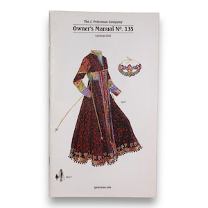 Może przedstawiać: Okładka instrukcji obsługi The J. Peterman Company nr 135, Karnawał 2016, przedstawia szczegółową ilustrację długiej, bogato zdobionej sukni z pasującym kołnierzem. Suknia jest głównie czarna z czerwonymi wzorami kwiatowymi i kolorowymi akcentami.