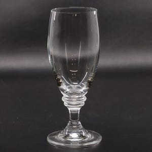 May include: A clear, stemmed glass with a rounded bowl and a detailed base. The glass has a slender stem and a circular foot. The bowl has vertical lines and a decorative design near the base. The glass is designed for beverages.