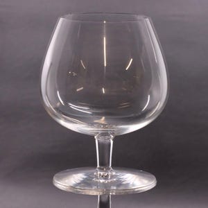 May include: A clear, stemmed brandy snifter glass. The glass has a rounded bowl and a short stem with a circular base. The glass is made of clear glass and is designed to hold brandy or other spirits.