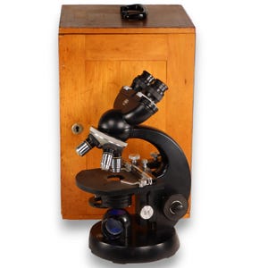 May include: A vintage black microscope with silver accents and a wooden storage case. The microscope has multiple lenses and adjustment knobs. The wooden case is light brown with a keyhole and a handle on top. The microscope is a scientific instrument.