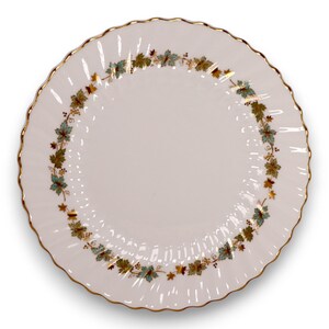 Può includere: Un piatto in ceramica bianca con bordo smerlato e bordo dorato. Il piatto presenta un bordo decorativo di foglie verdi, dorate e turchesi. Un classico della tavola.