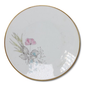 Op de afbeelding: Witte keramische plaat met een gouden rand en een bloemenontwerp. Het ontwerp toont een roze bloem, grijze bladeren en lichtblauwe accenten. De plaat is rond.