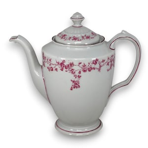 Puede incluir: Tetera de porcelana blanca con tapa y asa, adornada con un delicado estampado floral rosa. La tetera presenta un pico vertedor y una base con un ribete rosa a juego. Un diseño clásico para servir té.