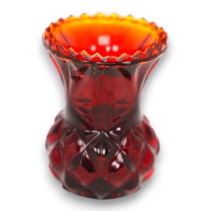 Può includere: Un vaso di vetro rosso rubino con un motivo a diamante strutturato. Il vaso ha una parte superiore svasata con un bordo smerlato e un interno arancione vibrante. Il vaso vintage è probabilmente utilizzato per scopi decorativi.