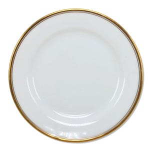 Puede incluir: Un plato de cerámica blanca con un borde dorado. El plato es redondo y tiene un diseño simple y elegante. El borde dorado añade un toque de lujo a la vajilla.