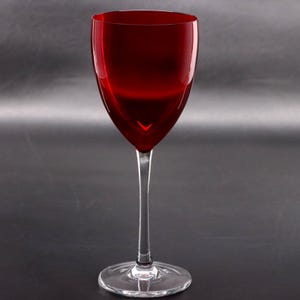 Puede incluir: Una copa de vino con un cáliz de color rojo intenso y translúcido de forma lisa y redondeada. El tallo y la base circular están hechos de vidrio transparente e incoloro, lo que crea un marcado contraste con el color rojo vibrante.