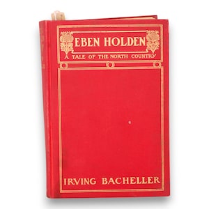 Puede incluir: Un libro rojo de tapa dura titulado "EBEN HOLDEN" con letras doradas y elementos decorativos. El nombre del autor, Irving Bacheller, también está en oro. Se ve un marcapáginas en la parte superior.