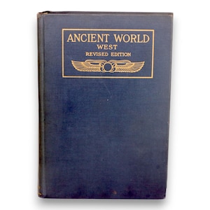 May include: A hardcover book titled "Ancient World West Revised Edition" in navy blue. The title is in a gold rectangular frame with a gold winged design. The book has a slightly worn appearance.