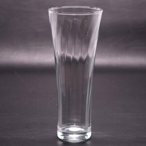 May include: A clear glass beer glass with a tall, slender shape and a textured, ribbed design.