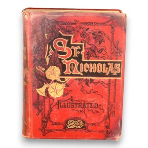 May include: Antique book titled "St. Nicholas Illustrated" with a red cover. The cover features ornate gold and black lettering, floral illustrations, and decorative borders. The book shows signs of wear, suggesting its age.