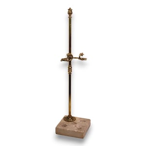 May include: An ornate brass stand with a square stone base. The stand features dragon-like figures and a finial at the top. The base has three circular indentations. The stand is likely for holding something. The height is approximately 100 cm.