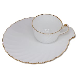 May include: A white porcelain teacup and matching snack plate set featuring a subtle spiral embossed pattern. Both pieces are finished with a delicate gold-painted scalloped edge. The cup includes a curved handle with gold trim details.