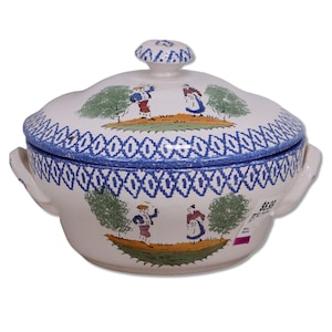 May include: A white ceramic serving dish with a lid, featuring a blue and white patterned rim and handle. The dish is decorated with illustrations of people and trees in a pastoral scene. The lid has a small knob.