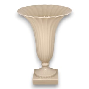 Puede incluir: Un florero de pedestal color crema con un borde ancho y festoneado y un cuerpo acanalado que se estrecha hacia un cuello delgado. El florero se asienta sobre una base cuadrada con un borde decorativo festoneado y un acabado liso y uniforme.