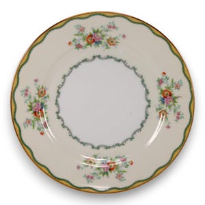May include: A cream-coloured plate with a scalloped edge and a gold border. The plate features floral bouquets in pink, orange, and blue, and a green and white decorative inner border. The centre of the plate is white.