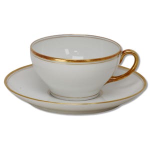 Puede incluir: Juego de taza y platillo blancos con ribetes dorados. La taza tiene forma redondeada con asa dorada. El platillo es redondo y combina con los ribetes dorados de la taza. Un diseño clásico para té o café.
