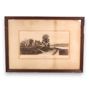 May include: A framed sepia-toned print depicting a rural landscape with a house, trees, and a winding road. The artwork is encased in a dark brown wooden frame, adding a classic touch to the scene. The print is likely an etching or engraving.