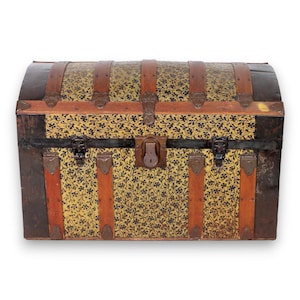 May include: A domed storage trunk featuring a yellow surface with a black floral pattern. The exterior is reinforced with vertical brown wooden slats, dark metal corner protectors, and a central metal latch mechanism with a keyhole.
