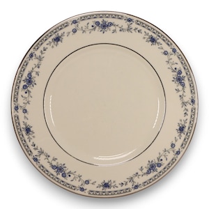 May include: A round, off-white plate with a delicate blue floral border and a silver rim. The plate features a black inner ring and a repeating floral pattern around the edge, suitable for formal dining.