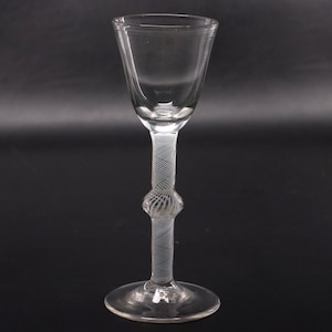 May include: A clear glass stemware piece featuring a flared bowl and a tall, slender stem. The stem is decorated with an intricate white latticino filigree pattern and includes a central spherical knop, supported by a circular glass base.
