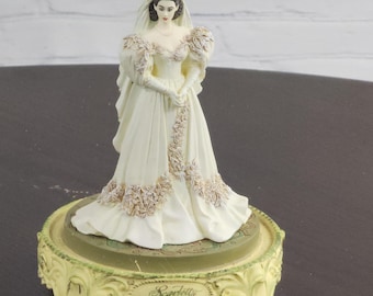Peut inclure: Une figurine en porcelaine blanche d'une mariée portant une robe blanche avec des détails floraux. La figurine est sur un socle jaune avec les mots "Scarlett Betrothed" inscrits dessus.