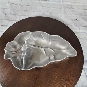 May include: A silver leaf-shaped serving dish made of pewter. The dish is on a dark brown wooden surface.
