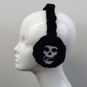 May include: Black earmuffs with a skull graphic. The earmuffs are black with a plush texture and feature a white skull design on each ear covering. The headband is also black and plush.