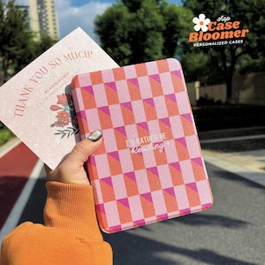 Peut inclure: Un étui à motifs géométriques roses et oranges avec le texte "I'D RATHER BE Reading" est tenu devant une carte de remerciement. L'étui est un produit personnalisé de Case Bloomer.