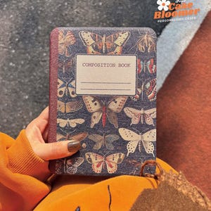 May include: A composition book with a dark blue cover featuring a pattern of colorful butterflies. The cover has the text "COMPOSITION BOOK" printed in white.