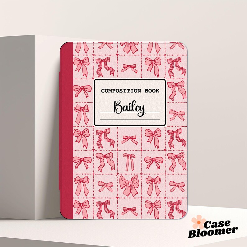 May include: Pink composition book with a red spine and a pattern of pink bows on a white background. The book says "COMPOSITION BOOK" and "Bailey" on the front.