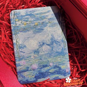 Könnte beinhalten: Eine Handyhülle mit einem blauen und weißen Gemälde von Seerosen. Die Hülle hat eine weiße Blume mit einem rosa Zentrum und den Text "shop Case Bloomer PERSONALIZED CASES".
