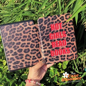 May include: An e-reader case with a leopard print design, open to show the red text "HOT GIRLS READ BOOKS". The case is brown with black spots. Green leaves form the background.