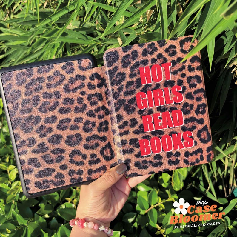 May include: An e-reader case with a leopard print design, open to show the red text "HOT GIRLS READ BOOKS". The case is brown with black spots. Green leaves form the background.