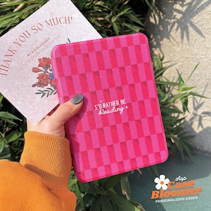 Peut inclure: Une coque rose et magenta à motifs avec le texte "I'D RATHER BE Reading +" est tenue à côté d'une carte de remerciement. L'étui a un motif en damier. La carte dit "THANK YOU SO MUCH!" et "YOUR ORDER MADE OUR DAY".