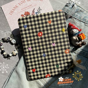 May include: A black and cream checked phone case adorned with embroidered hearts, stars, and flowers in various colours. The case rests on denim jeans. A snowman figurine and a bracelet are also in the image. The text "THANK YOU SO MUCH!" is visible.