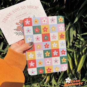 Puede incluir: Una funda colorida con estampado floral para un lector electr&oacute;nico. La funda tiene un patr&oacute;n de cuadros con cuadrados rojos, amarillos, verdes, azules y rosas. Cada cuadrado tiene una flor blanca con un centro amarillo.