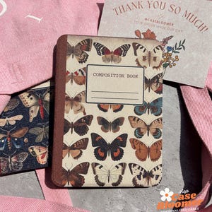 May include: A composition book with a brown cover featuring a pattern of colorful butterflies. The text "COMPOSITION BOOK" is printed on the front cover.