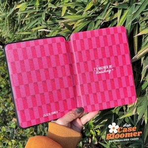 May include: A pink and black e-reader case with a chequered pattern. The case has the text "I'd rather be reading" printed on the front.