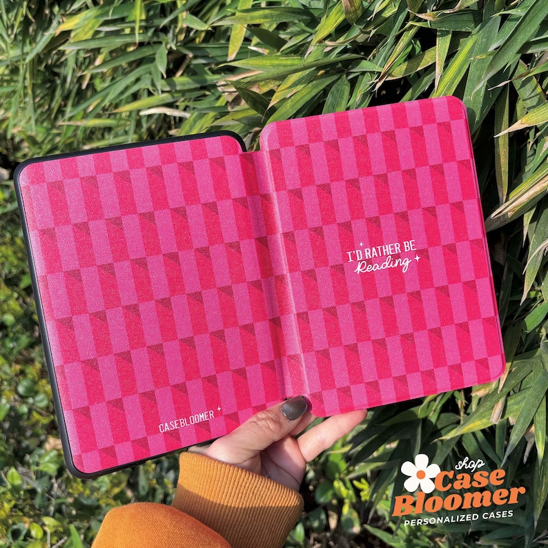 May include: A pink and black e-reader case with a chequered pattern. The case has the text "I'd rather be reading" printed on the front.