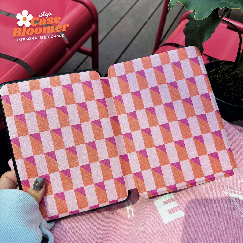 Puede incluir: Una funda para Kindle a cuadros rosa y naranja con el texto "shop Case Bloomer PERSONALIZED CASES" en la parte delantera.