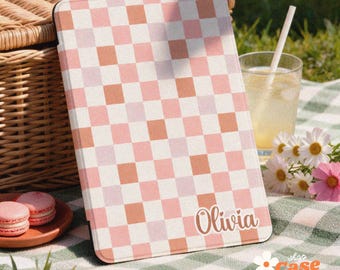 May include: A rectangular e-reader case featuring a repeating checkered pattern in shades of light pink, soft orange, and white. The name Olivia is printed in white cursive script in the bottom right corner of the case.