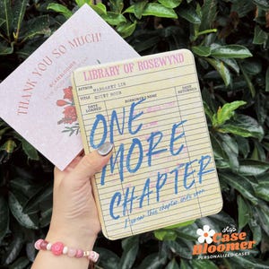 May include: A personalized phone case with a vintage library card design. The case features the text "ONE MORE CHAPTER" in blue, with the author's name and book title. A thank you card with floral accents is also visible.