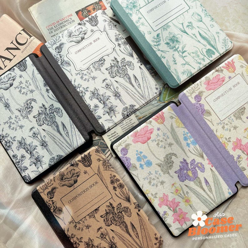 May include: Several composition book covers with floral designs. The covers display botanical illustrations of irises, roses, and other flowers. Some covers have the words "COMPOSITION BOOK" printed on them. The colour palette includes shades of beige, green, and purple.