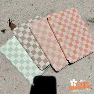 May include: Three checkered phone cases in different colors: green, brown, and pink. The cases have a subtle glitter finish and are arranged in a stack.