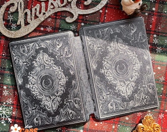 May include: A black and silver patterned book cover with a crescent moon design. The cover is made of a textured material and has a subtle sheen. The text "Shop Case Bloomer Personalized Cases" is visible in the bottom left corner.